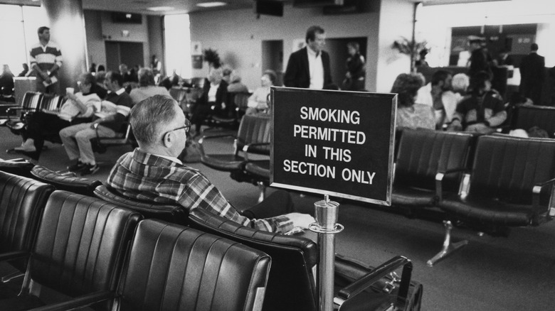 Black and white photo of people sitting in a smoking section at an airport in the 1980s