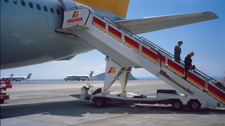 People walk off a retro Iberia plane from the 1980s onto a tarmac
