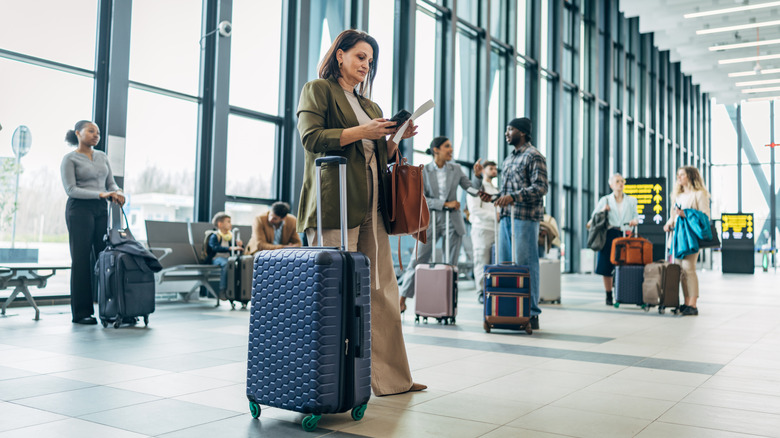 Travelers standing in an airport with their carry-on luggage