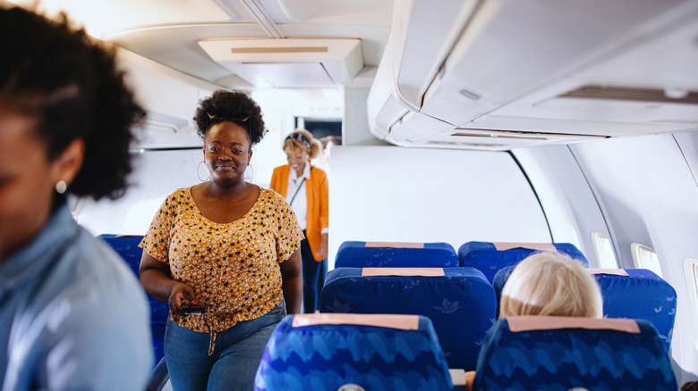 People boarding a plane, walking down the cabin aisle