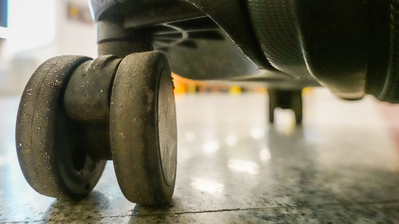 A close-up image of a dirty suitcase wheel on a floor