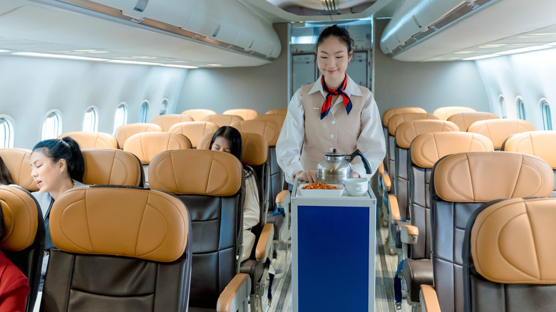 A flight attendant on a plane with a beverage cart