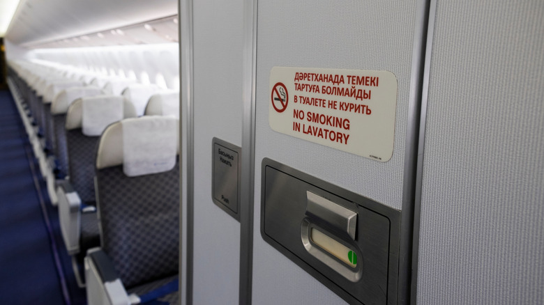 A lavatory in an airplane is pictured with rows of seating in the background.