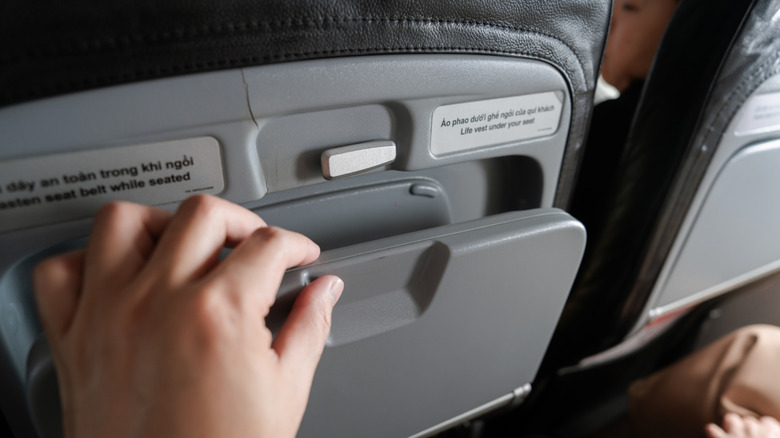 A hand unlatches and lowers an airplane tray table.