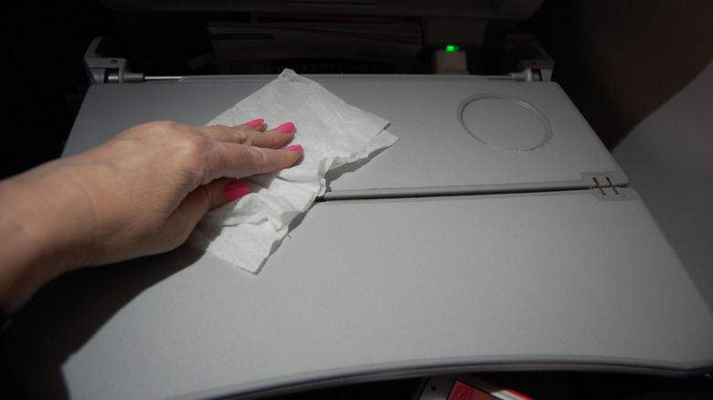A passenger with pink fingernails wipes an airplane tray table with a sanitizing wipe.