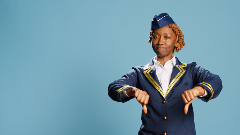 Stewardess dressed in aviation uniform rejecting something with a thumbs down.