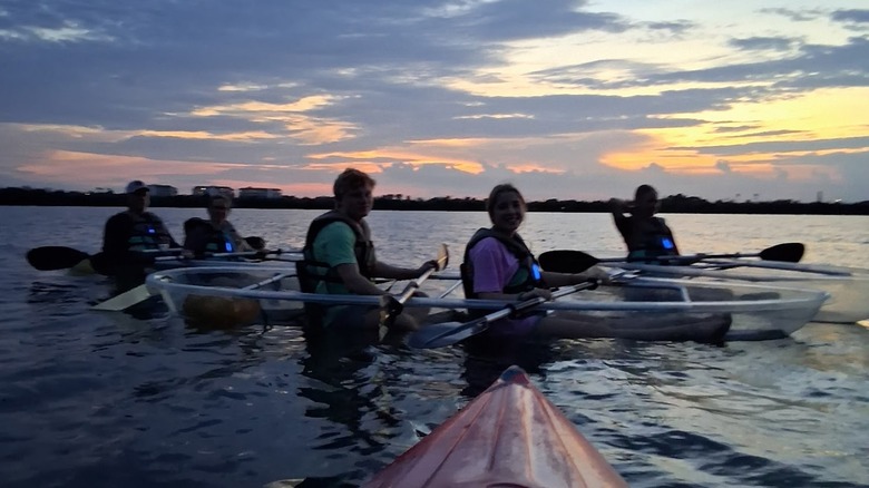 Kayakers and canoers on the waters off the Florida coast, with a dark sunset behind them