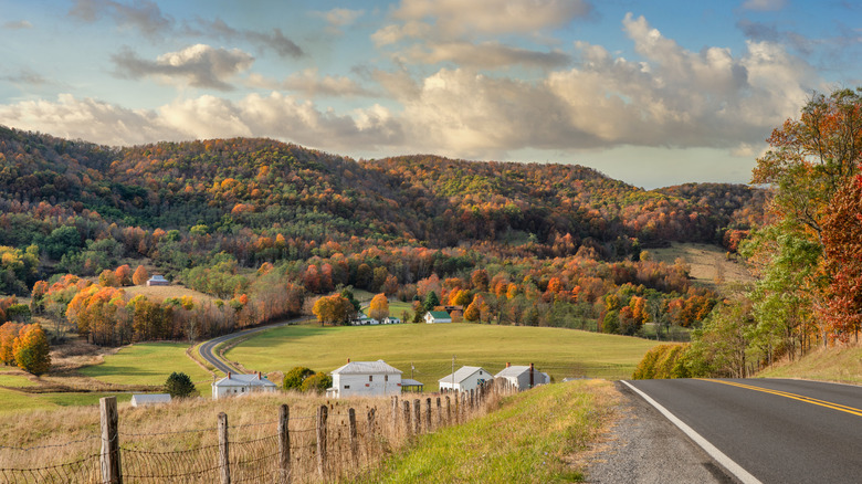 A road stretches alongside farmland, forest and mountains with fall foliage in Virginia