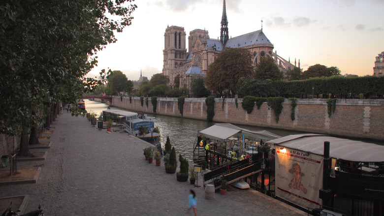 bank of the seine river with a floating cafe and notre dame in the background