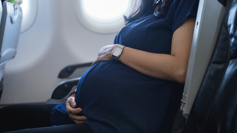 A pregnant woman sits in her seat on an airplane.