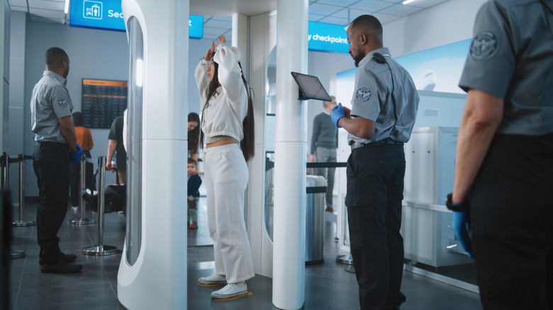 A woman stands with her hands above her head as she is screened by a full-body scanner in an airport security line.