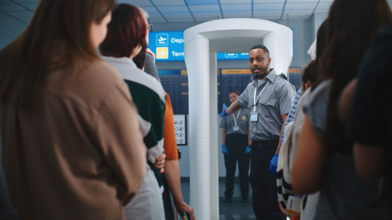 An airport security officer instructs passengers prior to passing through a metal detector.