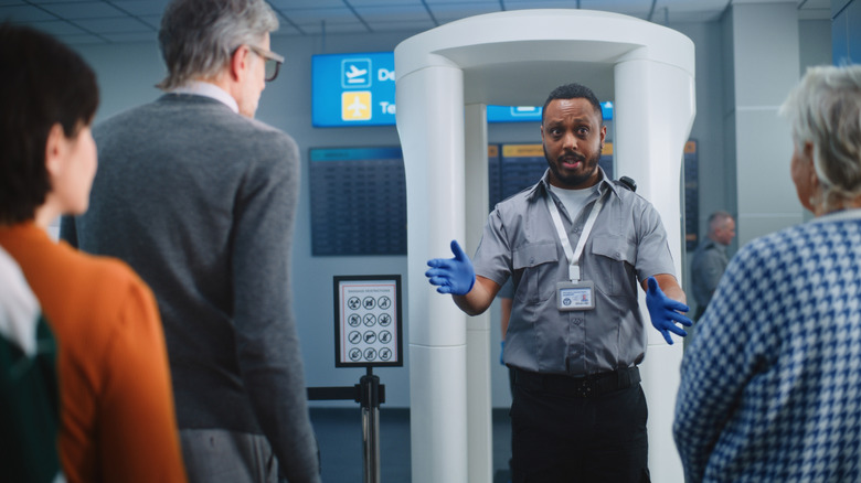 A security officer giving instructions to passengers using a body scanner at an airport