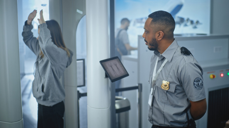 An airport security officer screening a woman in a body scanner at the airport security checkpoint