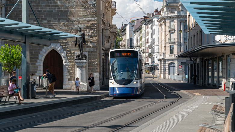 Lightrail tram train pulls into a station in Geneva, Switzerland with passengers waiting at the stop