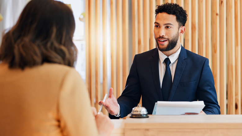A male hotel receptionist welcoming a female traveler
