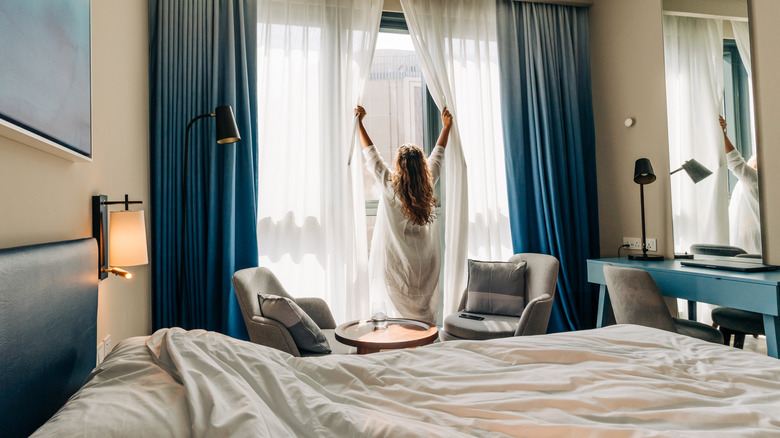 A woman opening curtains to look out her nice hotel room