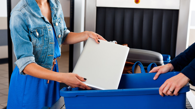 A woman placing a laptop inside a bin to be screened at a security checkpoint.