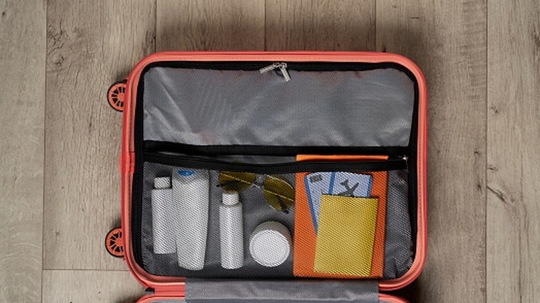 A mesh pocket on the inside of a carry-on suitcase filled with small tubes and papers.