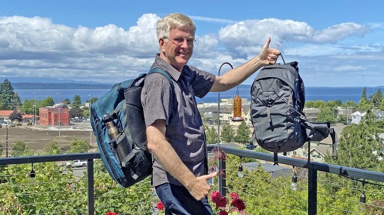 Rick Steves on a terrace holding two backpacks