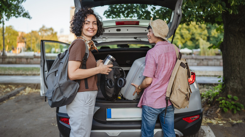 Two smiling friends packing the trunk of a car with luggage