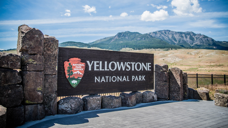 A sign reads "Yellowstone National Park" with plains and mountains in the background