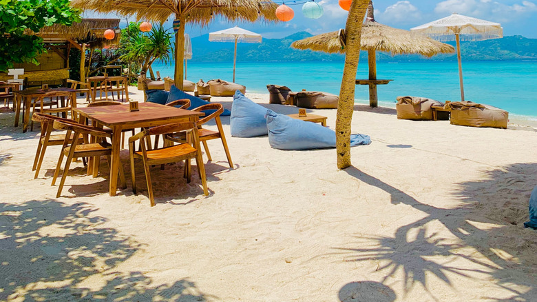 Sunny morning at a Cafe on Gili Air Island, Indonesia featuring paper lanterns, thatched umbrellas, and blue water in the background