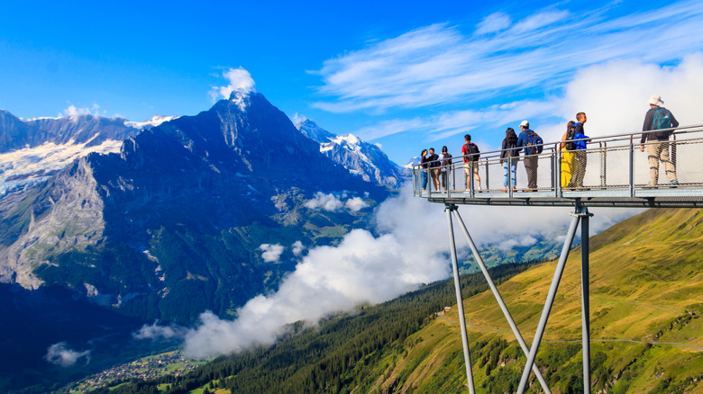 People standing on a long and narrow viewing platform with snowcapped mountains in background