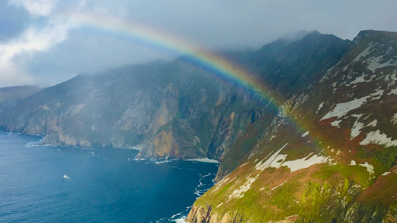 Sliabh Liag Cliffs with rainbow in foreground and cloudy sky.