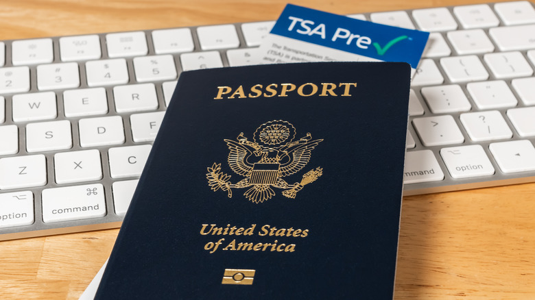US Passport with Department of Homeland Security TSA Pre Check registration information card on a desk with computer keyboard.
