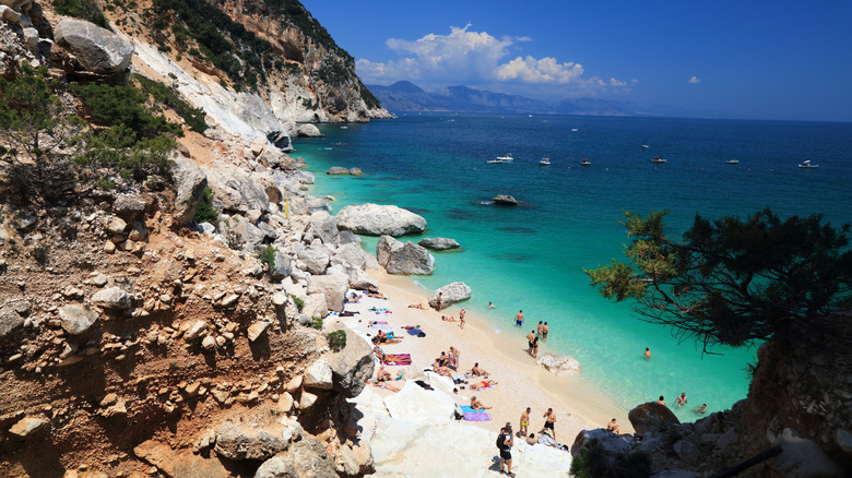 Cala Goloritzé in Sardinia, Italy, with people lounging on the sand and swimming in the water
