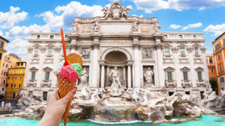 A tourist holds up a cone of gelato in front of the Trevi Fountain in Rome
