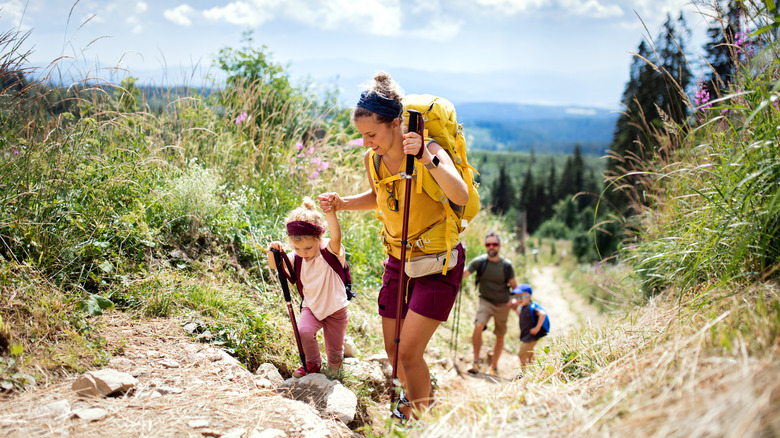 A happy family helping one another climb a hill while hiking