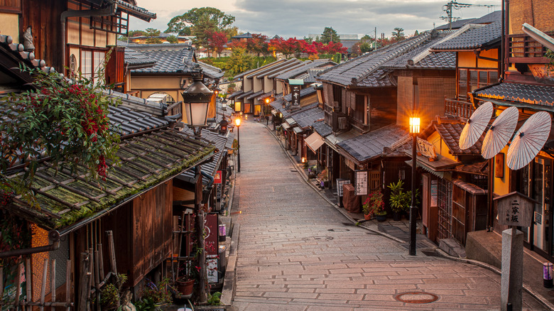 View of a traditional street in Kyoto, Japan with residences, tea houses, and shops with autumn foliage in the background