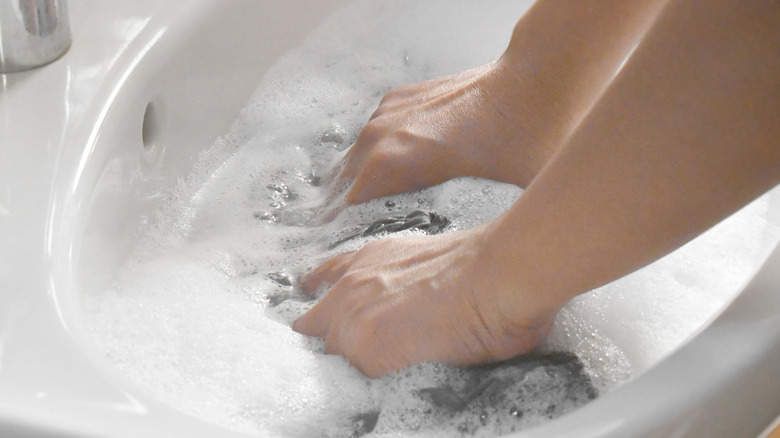 Hands washing clothes in a white sink with suds