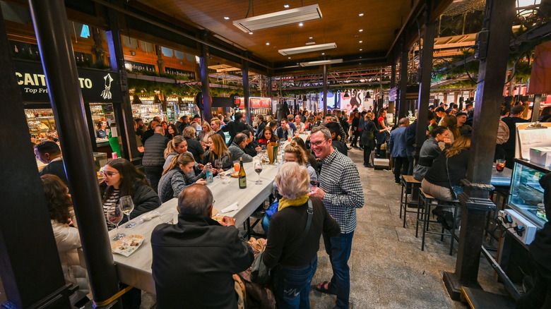 crowds of people eating and talking around standing tables at an indoor market