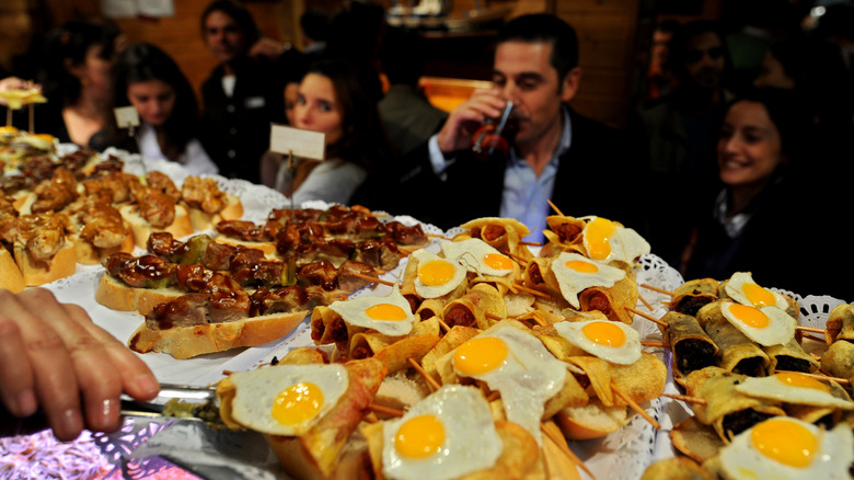 rows of tapas on display with people eating in the background
