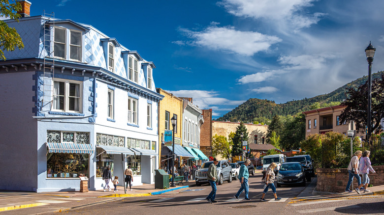 people crossing a small intersection with a block of shops behind them and mountains in the background