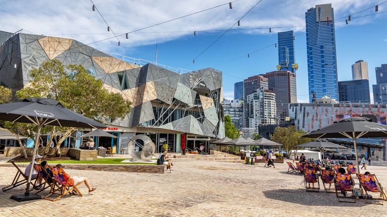 People enjoy the summer weather amid bold architecture and skyline views in Federation Square, Melbourne, Australia