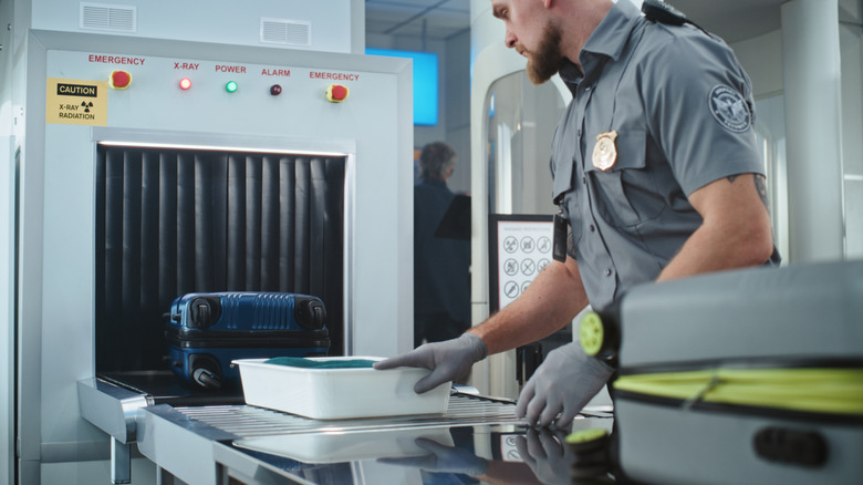 An airport security officer moving luggage through an x-ray machine