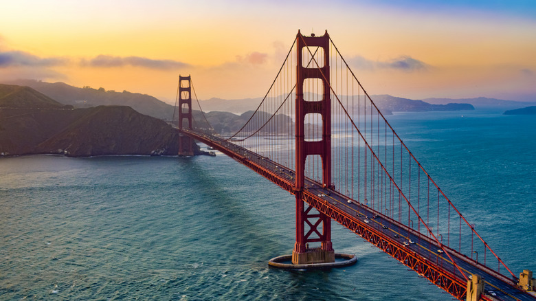 The Golden Gate Bridge against a vivid orange sunset, with mountains in the distance.