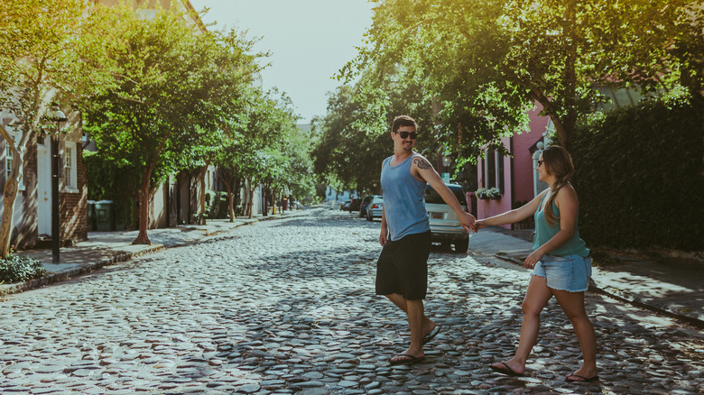 Couple holding hands as they walk down a covered street lined with pastel homes in Charleston, South Carolina