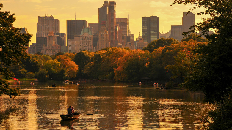 Couple rowing in a rowboat on a lake in Central Park under the New York skyline during an autumn sunset