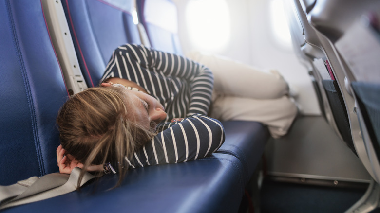 A woman sleeps across multiple seats on an airplane.