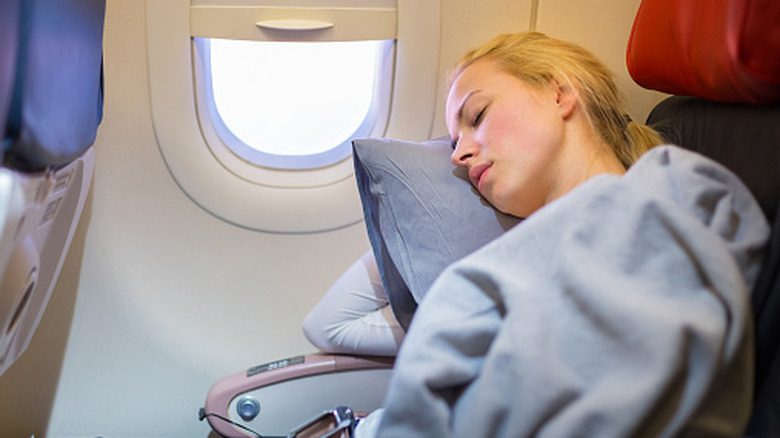 A woman sleeps in a window seat on an airplane.