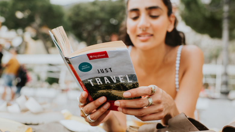 A woman holds and reads a travel guide book.