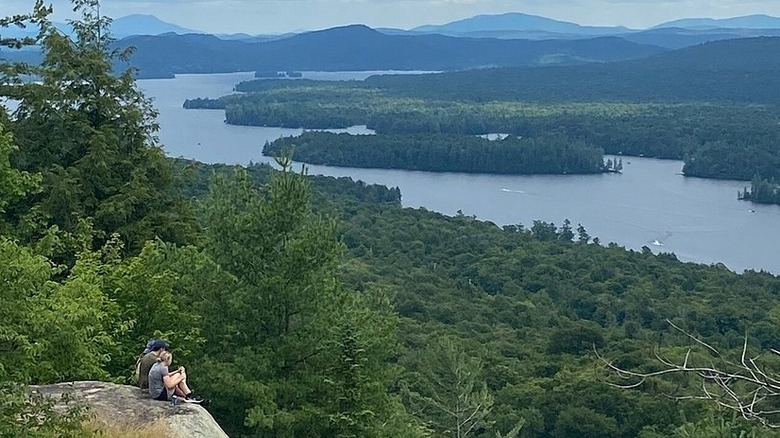 a couple on a cliff's edge looking at panoramic view of forested mountains  and lakes