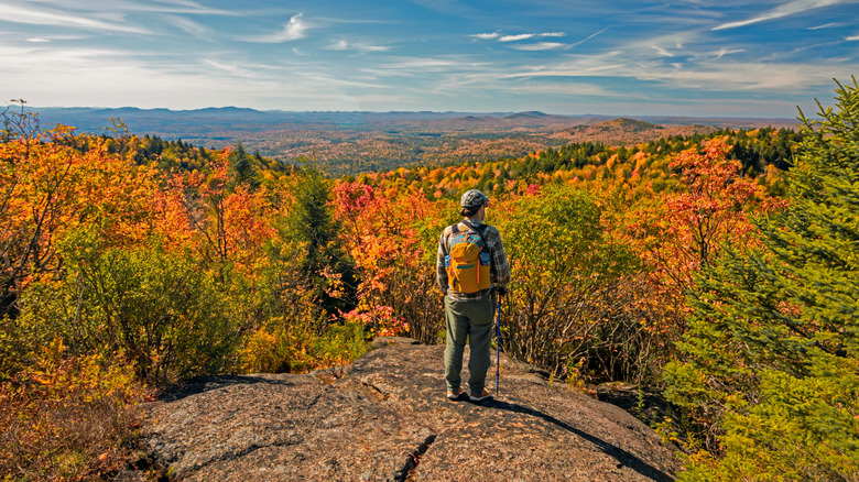 hiker at mountain summit overlooking changing fall leaves