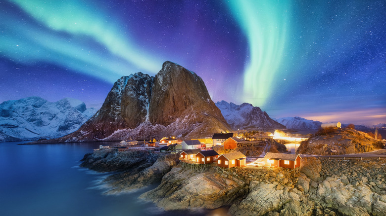 Fishing cabins on Lofoten Island with snowy mountains and bright northern lights.