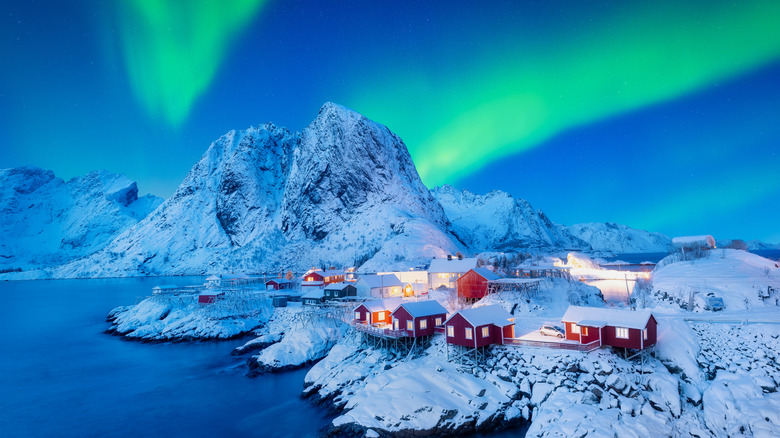Red fishing houses on the Lofoten Islands, covering in snow, under the green Northern Lights